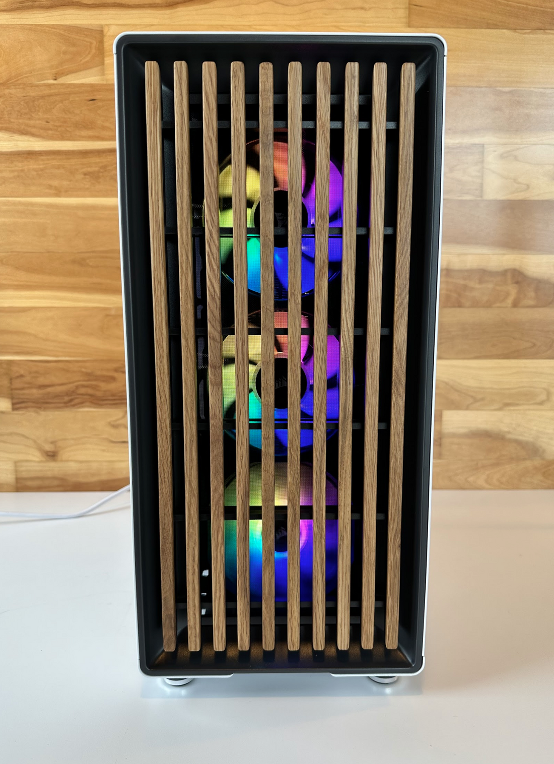A white custom gaming PC built by DC Computers with a wood-slat front panel and RGB fans glowing through, on a wood-wall background